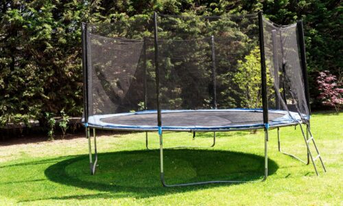 Trampoline with safety net set on grass, surrounded by trees, emphasizing the importance of stability and safety in backyard play equipment maintenance.