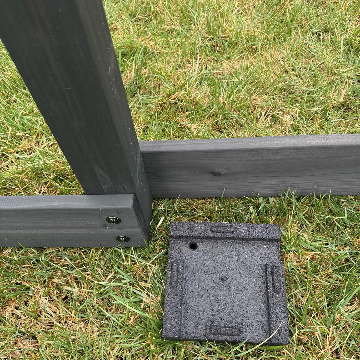 Large block positioned under sandbox board support, grass background, installation of LevelDry protective solution for outdoor play equipment.