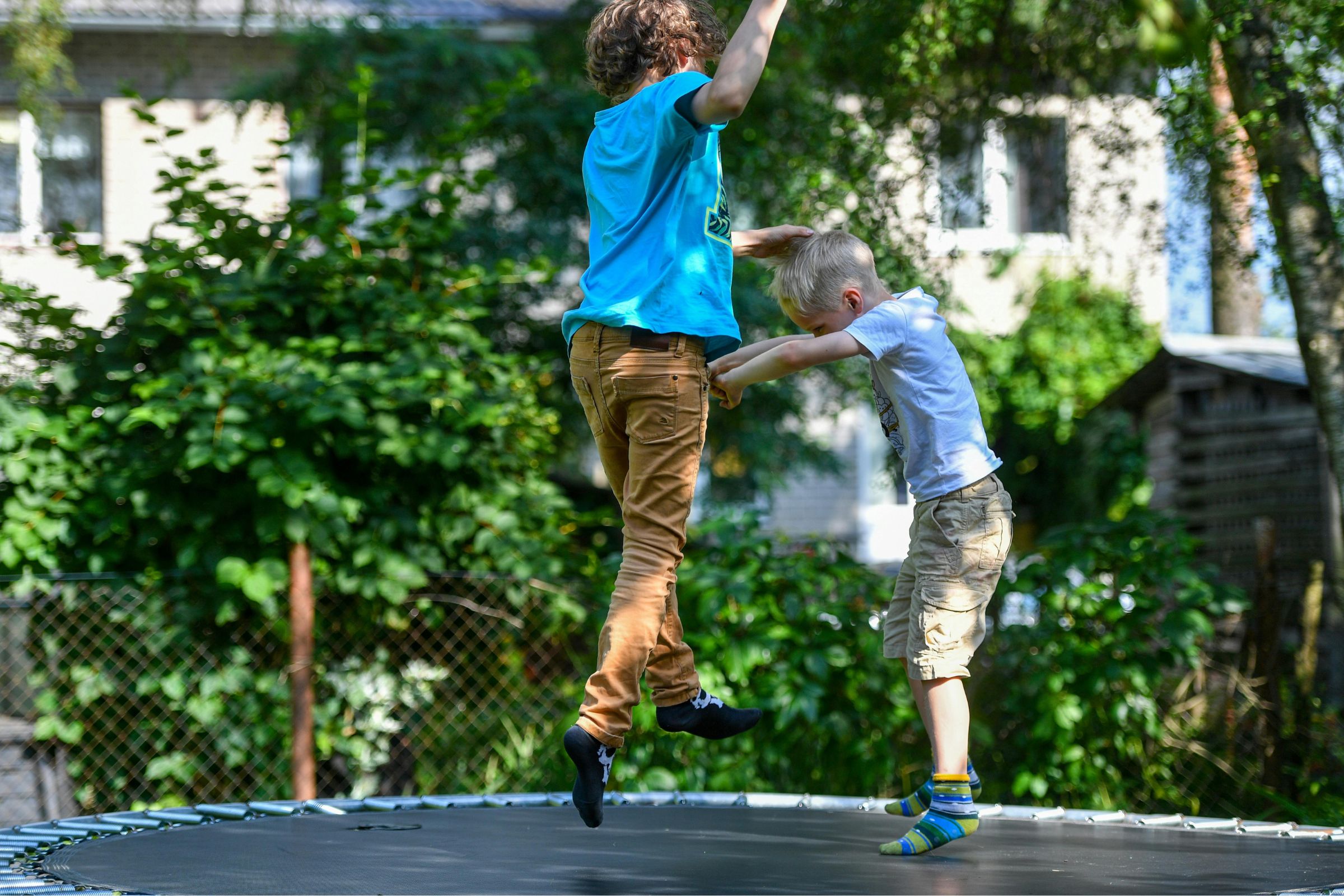 Children jumping on a trampoline surrounded by greenery, illustrating outdoor fun and play, relevant to maintaining level trampolines.